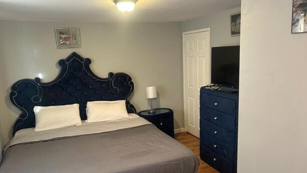 A bedroom with a bed, a dresser, a nightstand, a television, and a door. - Grove 3 (Irvington)