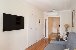 A living room with a flat-screen TV mounted on the wall, a wooden floor, and a grey sofa.
