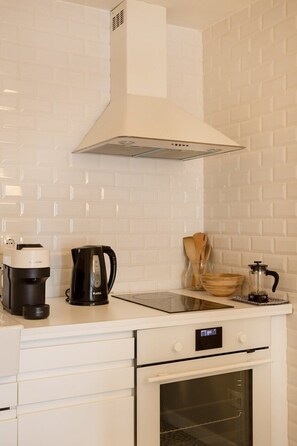 A kitchen with a white tiled backsplash, a coffee maker, a kettle, a wooden bowl, and a coffee grinder on the counter. - Bright Alfama Studio with AC (Lisbon)