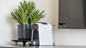 A coffee machine on a table with a potted plant beside it.