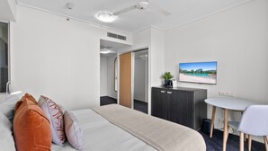 A hotel room with a bed, bedside table, desk, chair, and a TV on the wall.