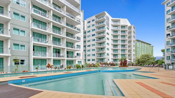 A modern hotel with multiple floors, a central swimming pool, and outdoor seating areas.