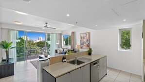 Una cocina moderna con una isla grande, un comedor con sofá y mesa, y un balcón con vista a la ciudad.