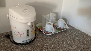 A coffee maker with a power cord, two white cups, and a tray with coffee packets on a granite countertop. - Easarninn Yasothorn (Yasothon)