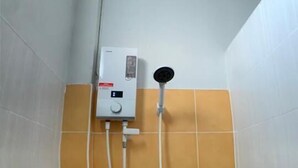 A small, enclosed shower area with a built-in heater, a handheld showerhead, and a soap dispenser. - Easarninn Yasothorn (Yasothon)