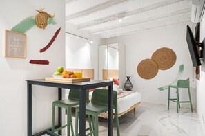 A modern, well-lit room with a dining table, chairs, a bed, and a mirror. - Dobohomes D14 (Madrid)