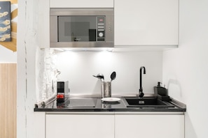A modern kitchen with a stainless steel microwave, a sink, and a compact stove. - Dobohomes D14 (Madrid)