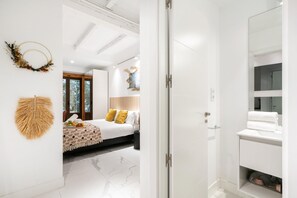 A modern hotel room with a bed, a bathroom with a mirror, and a view of trees through the window. - Dobohomes D14 (Madrid)