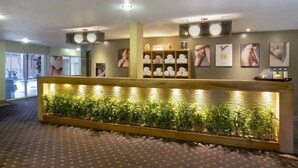A reception area with a wooden reception desk, a plant display, and framed pictures on the wall. - Forest Pines Spa and Golf Resort (Brigg)