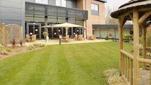 A modern building with a patio area featuring outdoor seating and a thatched-roof structure. - Forest Pines Spa and Golf Resort (Brigg)