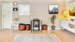 Una sala de estar moderna con chimenea, un reloj, un cuadro enmarcado, una planta en maceta y una lámpara.