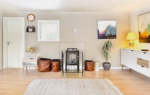 Una sala de estar moderna con chimenea, un reloj, un cuadro enmarcado, una planta en maceta y una lámpara.