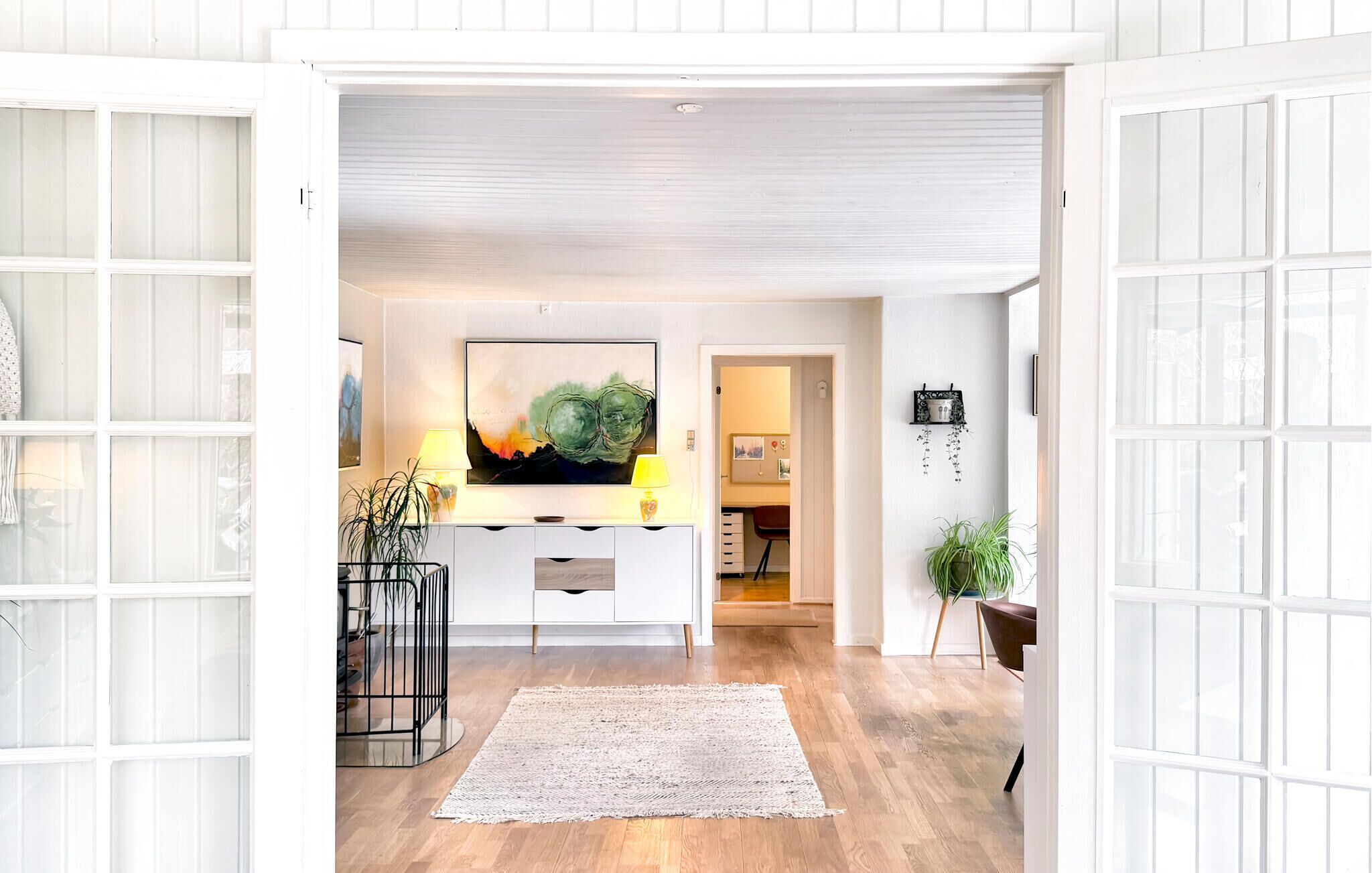 Un intérieur moderne avec un plancher en bois, une console centrale, une grande peinture abstraite et une plante en pot.