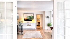 Un interior moderno con piso de madera, una consola central, un cuadro abstracto grande y una planta en maceta.