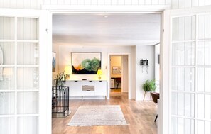 Un intérieur moderne avec un plancher en bois, une console centrale, une grande peinture abstraite et une plante en pot.