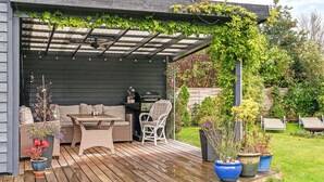 Un patio techado con una mesa y sillas de madera, una parrilla y plantas en macetas.