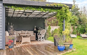 Un patio techado con una mesa y sillas de madera, una parrilla y plantas en macetas.