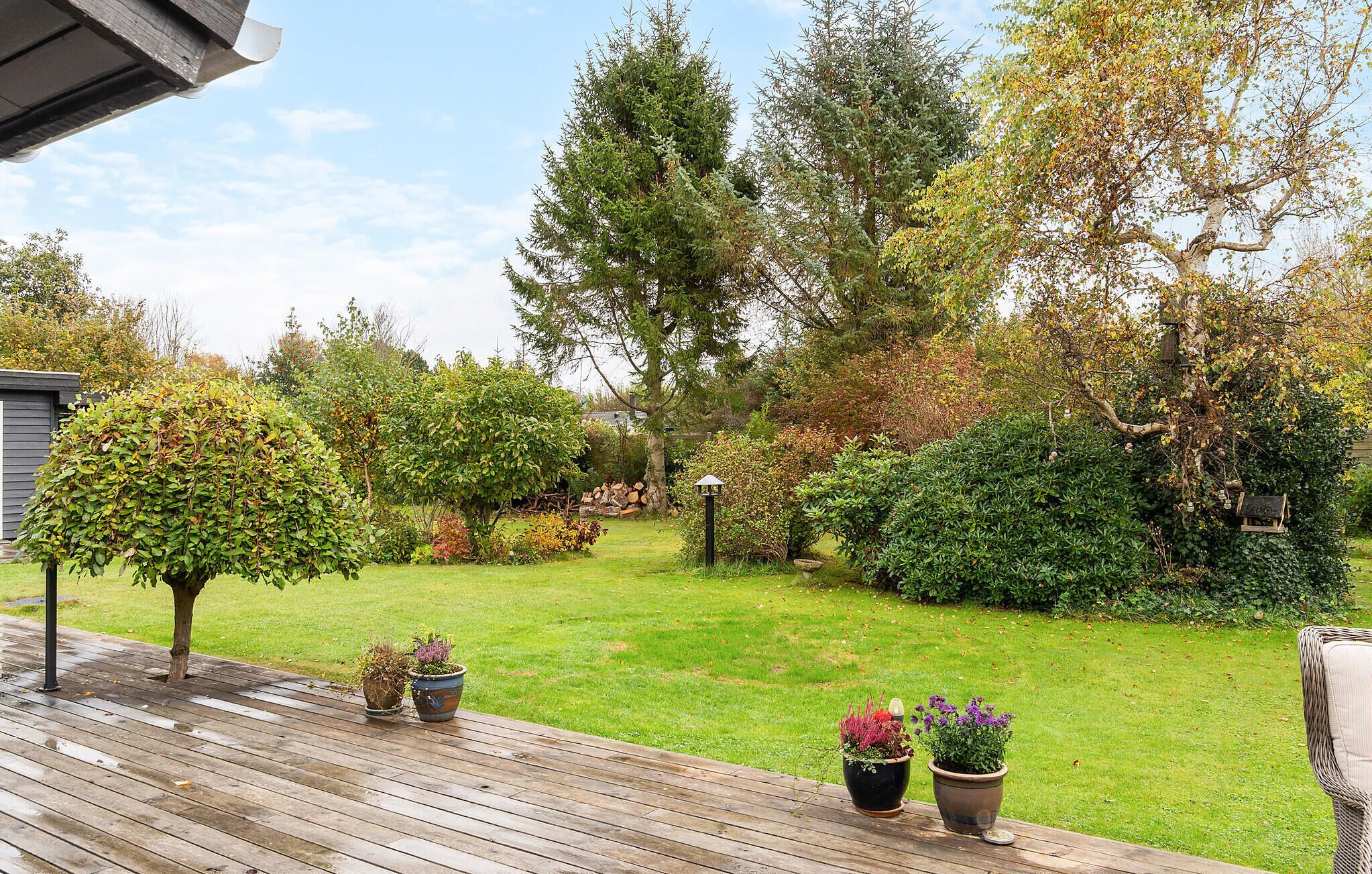 A wooden deck with potted plants and a grassy garden area with various trees and shrubs.