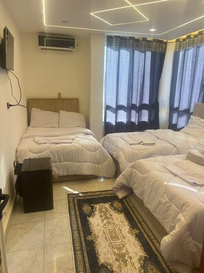 A hotel room with two beds, a TV mounted on the wall, an air conditioning unit, and a patterned rug on the floor. - Miracle Pyramids Hotel (Giza)