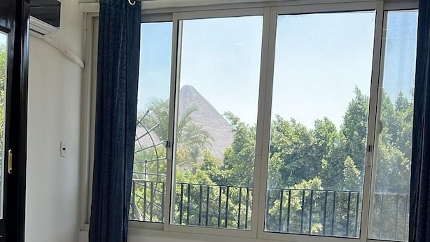 Ein modernes Schlafzimmer mit einem großen Bett, Blick auf Bäume und einen Berg durch das Fenster sowie ein Balkon mit Geländer.