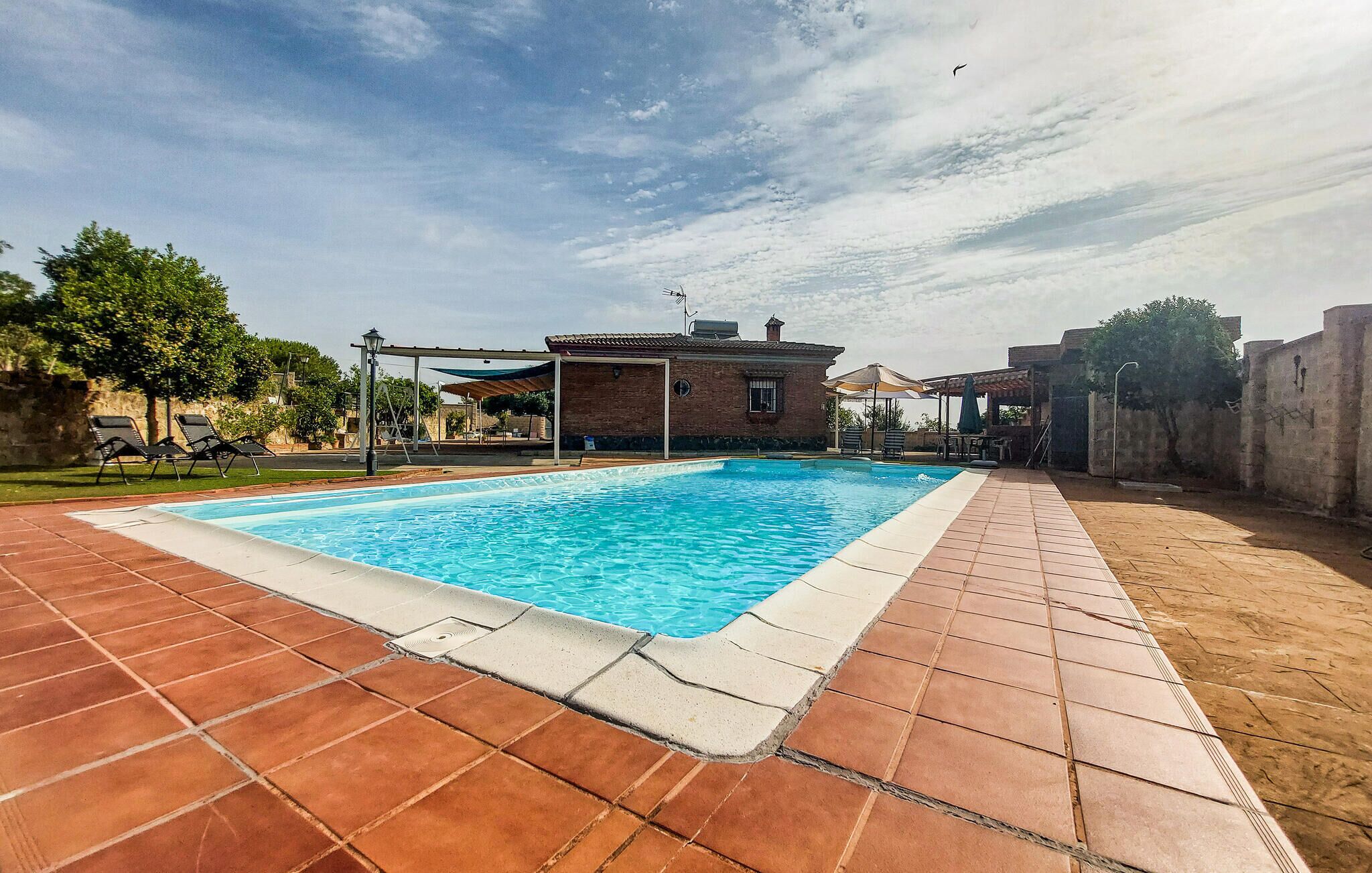 A rectangular swimming pool with a tiled deck, a brick building, and a clear sky.
