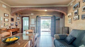 Un coin repas avec une table et des chaises en bois, un saladier de fruits et une arche en briques donnant sur une terrasse.