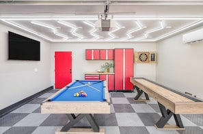 A pool table with billiard balls, a dartboard, and a dartboard in a room with a checkered floor, red cabinets, and a mounted TV. - Element By Avantstay Pool Firepit Game Room (Scottsdale)