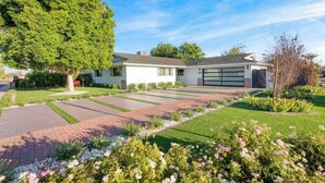 A modern two-story house with a garage, a well-maintained lawn, and a variety of flowering plants.