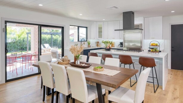 A modern kitchen with white cabinets, a central island, and a dining area with white chairs.