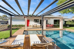 A pool area with lounge chairs, a covered patio, and a red door. - Element By Avantstay Pool Firepit Game Room (Scottsdale)