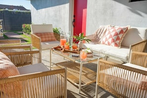 An outdoor seating area with wicker chairs and a glass table, a red door, and a white sofa with patterned cushions. - Element By Avantstay Pool Firepit Game Room (Scottsdale)