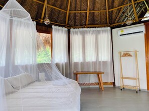 Ein Zimmer mit einem Bett unter einem Moskitonetz, Holzmöbeln und einer Klimaanlage.