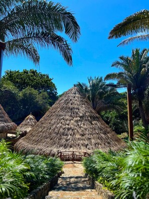 A thatched-roof structure surrounded by lush greenery and a clear blue sky. - Zirwa Hotel Boutique (Santa Marta)