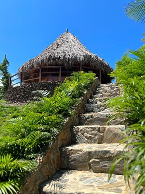 A thatched-roof building with a stone staircase leading up to it, surrounded by lush greenery. - Zirwa Hotel Boutique (Santa Marta)