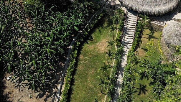 Luftaufnahme eines Resorts mit strohgedeckten Hütten, umgeben von üppiger tropischer Vegetation und einem klares Gewässer.