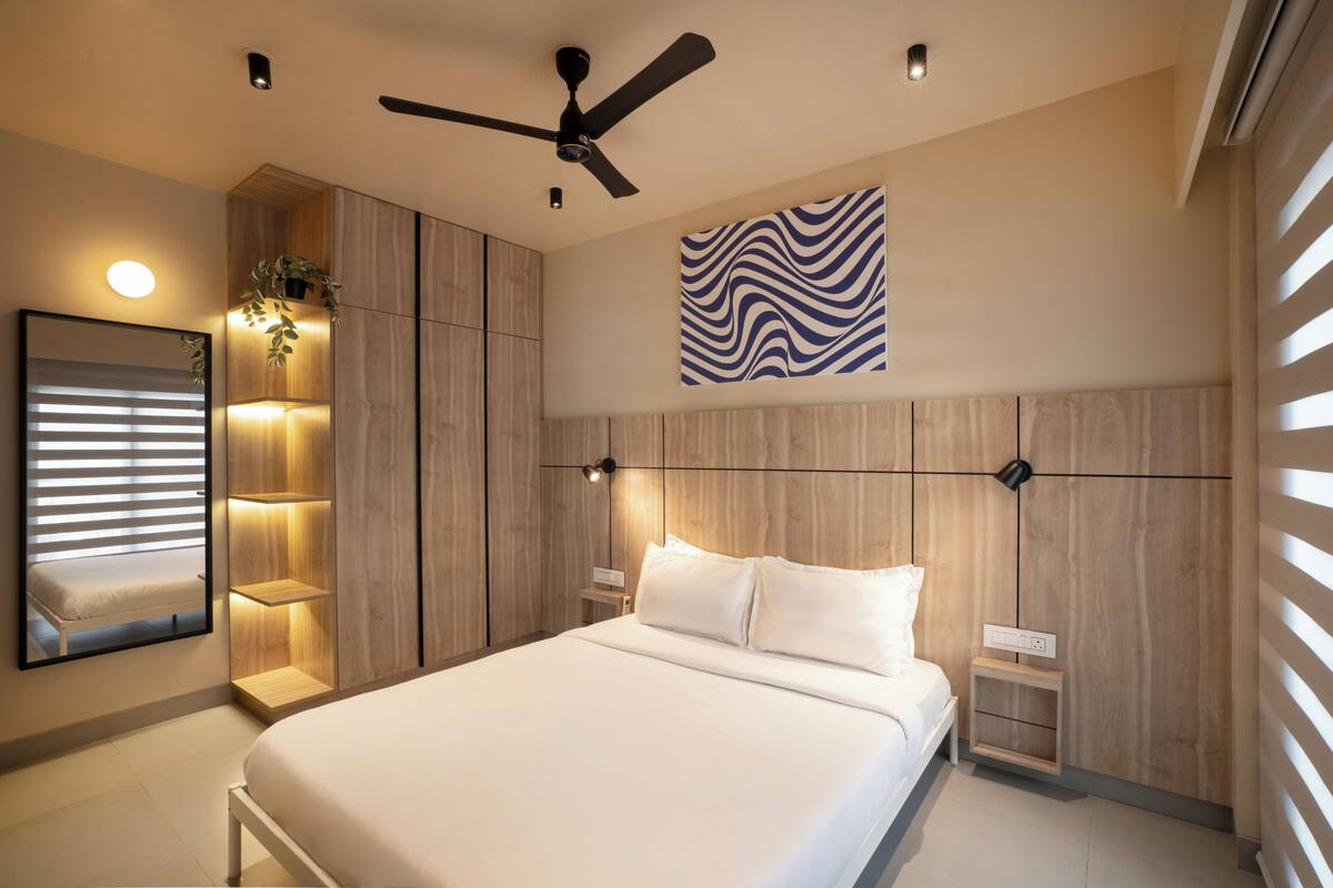Ein modernes Schlafzimmer mit Bett, Nachttischen, Deckenventilator, Wandleuchte und einem großen Spiegel.