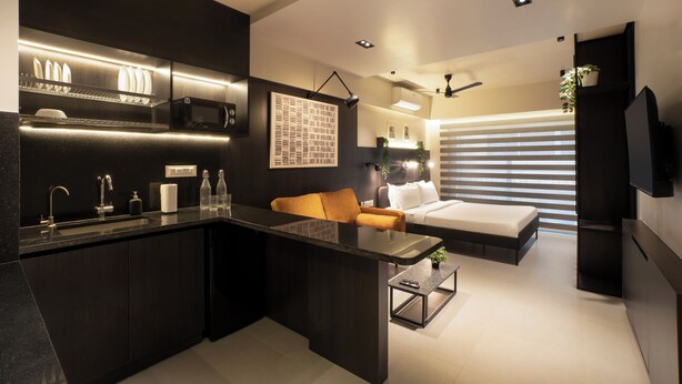 A modern kitchen with a dining area, a bed, and a TV. - Hotel PXL 27 (Bengaluru)