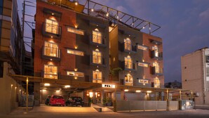 A multi-story hotel with a covered parking area, multiple balconies, and a visible entrance sign. - Hotel PXL 27 (Bengaluru)