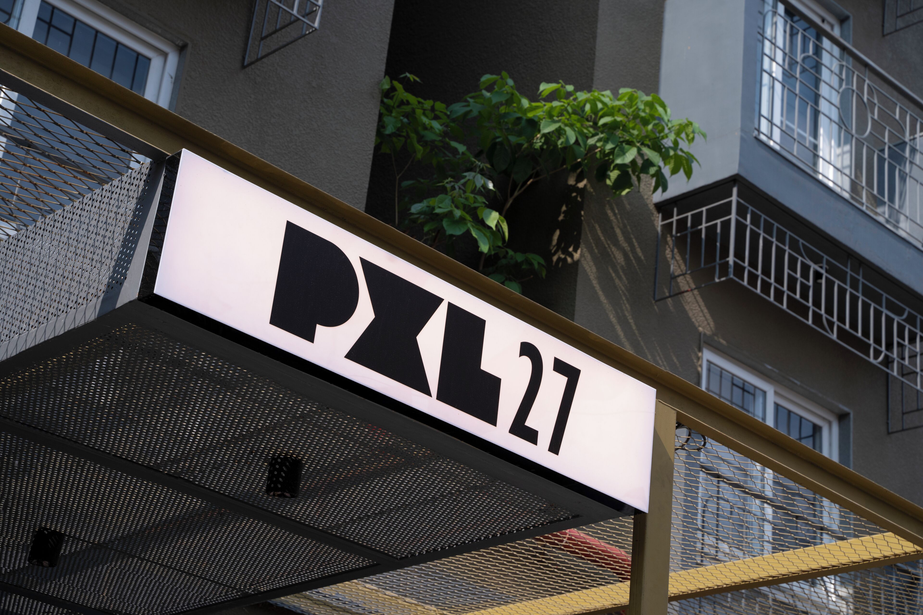 Un edificio con un cartel que dice 'PXL27' y una barrera de seguridad de malla.