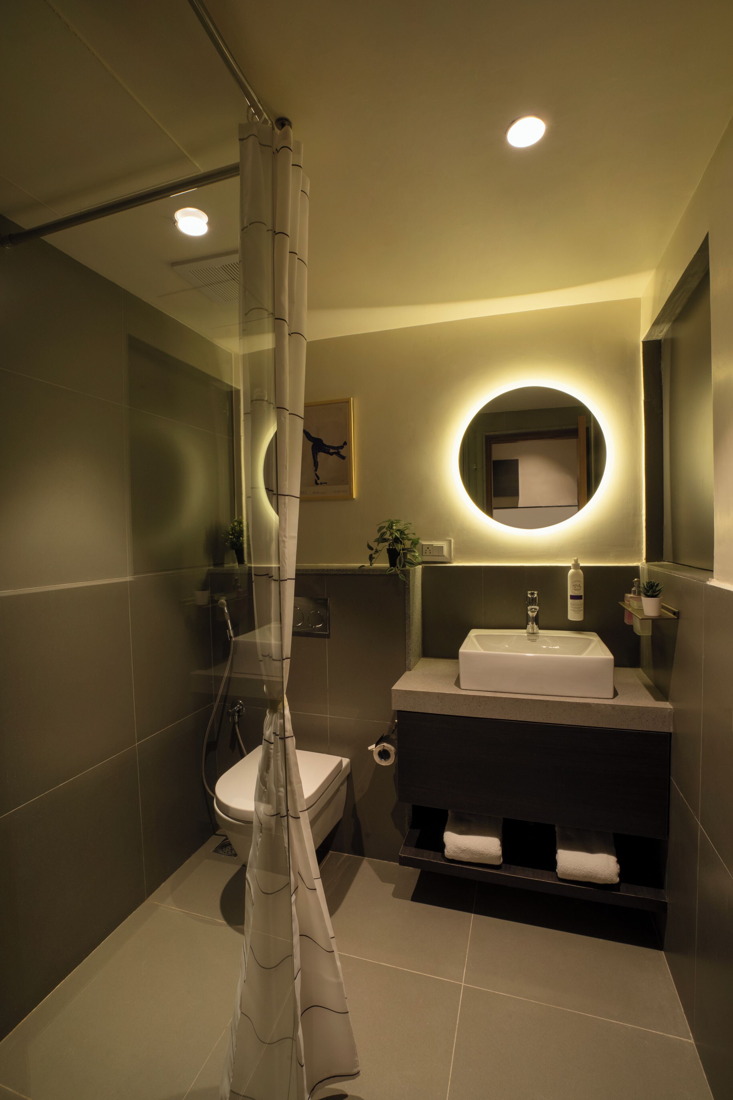 Une salle de bain moderne avec un rideau de douche, un lavabo, des toilettes et un miroir doté d’un éclairage circulaire.