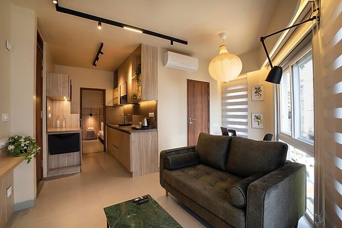 A modern kitchen with a dining area, a sofa, and a window with blinds.