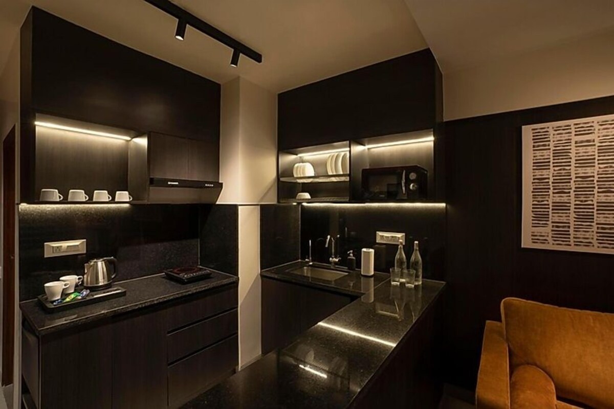 A modern kitchen with dark cabinetry, a stainless steel island, and a seating area with a brown chair.