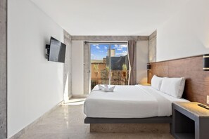 Une chambre d’hôtel avec un lit, un téléviseur fixé au mur et une vue sur l’extérieur par une fenêtre.