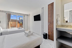 Une chambre d’hôtel avec deux lits, une télévision, une porte en bois et une salle de bain équipée d’un lavabo et d’un miroir.