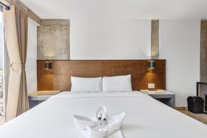 Een hotelkamer met een groot bed, een houten hoofdbord, twee nachtkastjes met lampen en uitzicht op het groen.