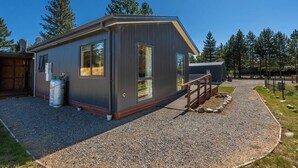 Eine moderne, eingeschossige Holzhütte mit grossen Fenstern, einer Schotterauffahrt und einer Holzterrasse.