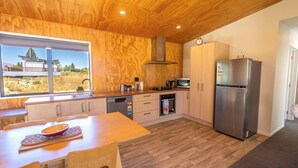 Eine moderne Küche mit Holzschränken, einem Edelstahlkühlschrank und Blick ins Grüne durch große Fenster.