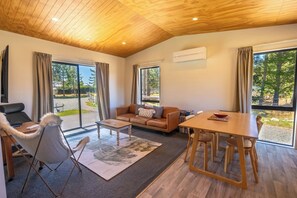 Una sala de estar moderna con techo de madera, un sofá de cuero, una mesa de comedor y ventanas amplias que ofrecen vistas al exterior.