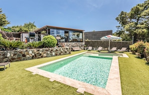 A backyard with a swimming pool, lounge chairs, and a stone wall.