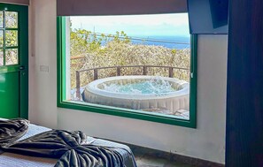 Habitació amb finestra gran que dona a una banyera d'hidromassatge i vista al mar.